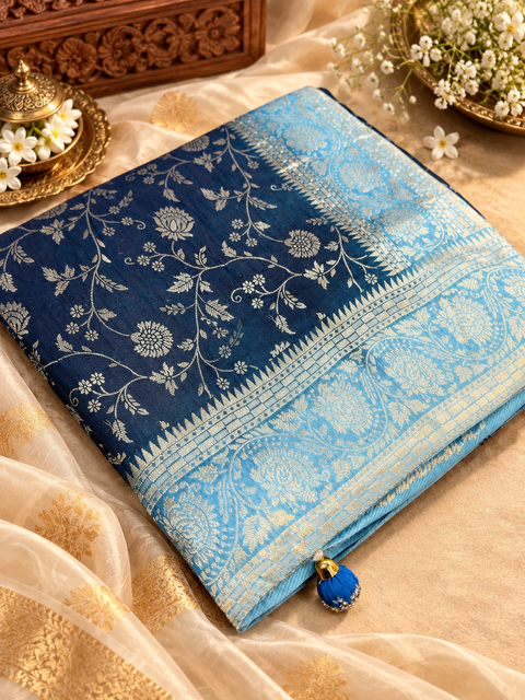 Dola Silk Saree with elegant all-over floral zari weaving and a rich contrasting woven border with detailed pallu. Soft, graceful drape with a luxurious festive look. Contrast blouse piece included.Slight variation in colour and design is possible.