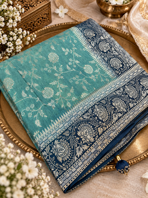Dola Silk Saree with elegant all-over floral zari weaving and a rich contrasting woven border with detailed pallu. Soft, graceful drape with a luxurious festive look. Contrast blouse piece included.Slight variation in colour and design is possible.