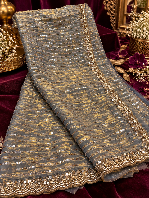 Grey & Gold Heavy Tissue Silk Saree – A luxurious Fendi silk and gold tissue blend featuring all-over sequin & hand work.Comes with an attached blouse piece,the blouse worn by the model is for reference only. Slight variation in colour & design may occur