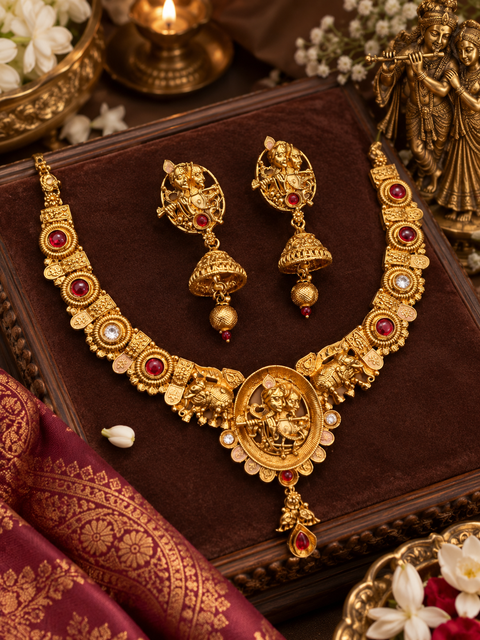Elegant matte gold-finish Temple Jewellery Set featuring an intricate Radha Krishna motif with beautifully detailed elephant designs and Ruby stone accents. Comes with matching jhumka earrings(slight variation in color & design may occur)