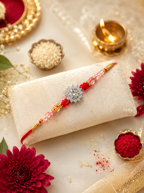 Elegant American Diamond Rakhi featuring a sparkling floral centrepiece, beautiful red and pink beads, and delicate gold accents. A perfect blend of traditional charm and timeless elegance for a special Raksha Bandhan celebration.