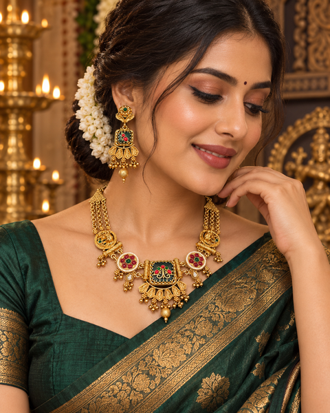 Elegant South Indian temple-style necklace set in a rich gold finish, detailed with red and green stones, pearl drops, and intricate traditional motifs. Comes with matching statement earrings(slight variation in color & design may occur)