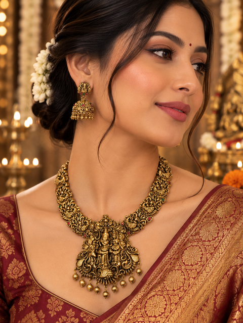 Elegant matte gold-finish Temple Jewellery Set featuring an intricate Krishna motif with beautifully detailed elephant designs and green stone accents. Comes with matching jhumka earrings(slight variation in color & design may occur)