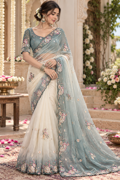 Smoky blue & ivory ombre shimmer organza saree with peacock floral handwork and scalloped border. Blouse worn by model is for reference only; actual blouse piece is attached. Slight variation in colour and design is possible.