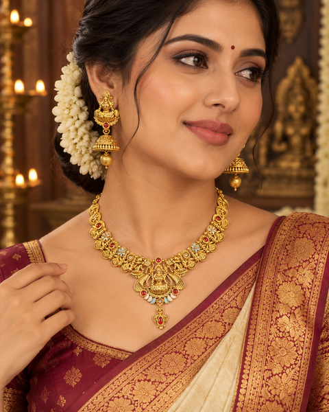 Elegant matte gold-finish Temple Jewellery Set Goddess Lakshmi  motif with beautifully detailed elephant designs and green ,Ruby stone accents. Comes with matching jhumka earrings(slight variation in color & design may occur)