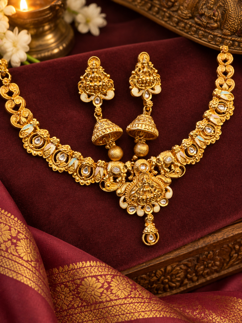 Elegant matte gold-finish Temple Jewellery Set Goddess Lakshmi  motif with beautifully detailed elephant designs and stone accents. Comes with matching jhumka earrings(slight variation in color & design may occur)